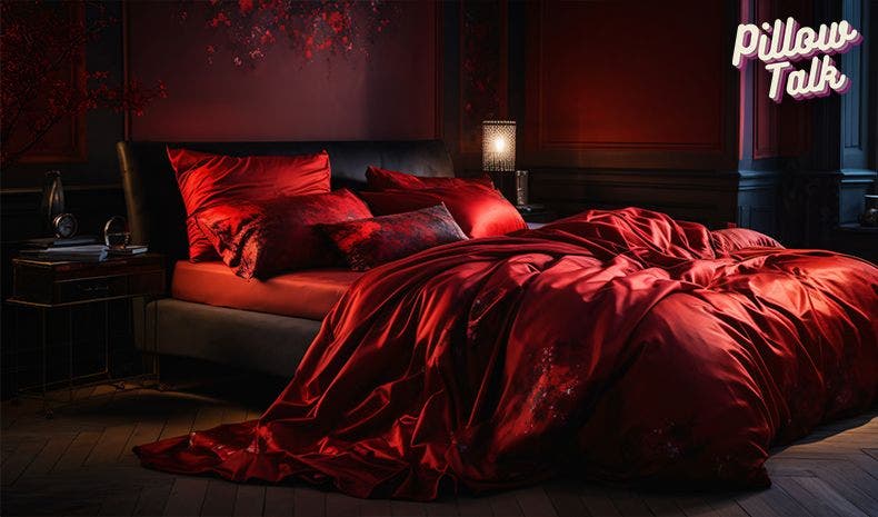 A dark sexy bedroom with a large bed draped with luxurious red silk bedding