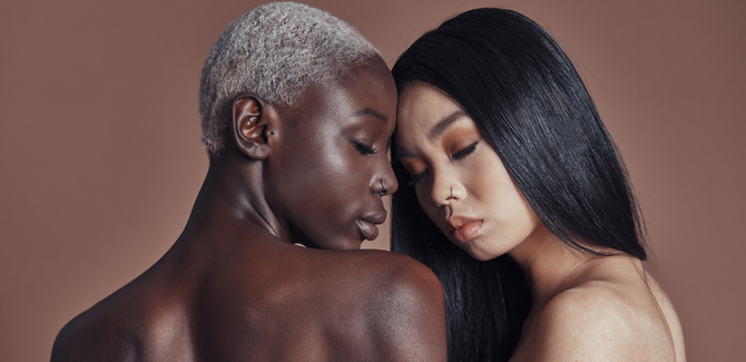 Black femme couple intimately embraced with their foreheads slightly touching. Their eyes are closed and appear to be naked, but only shoulders and up are visible.